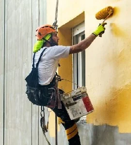 A rope-access painter applying finish to a building facade.